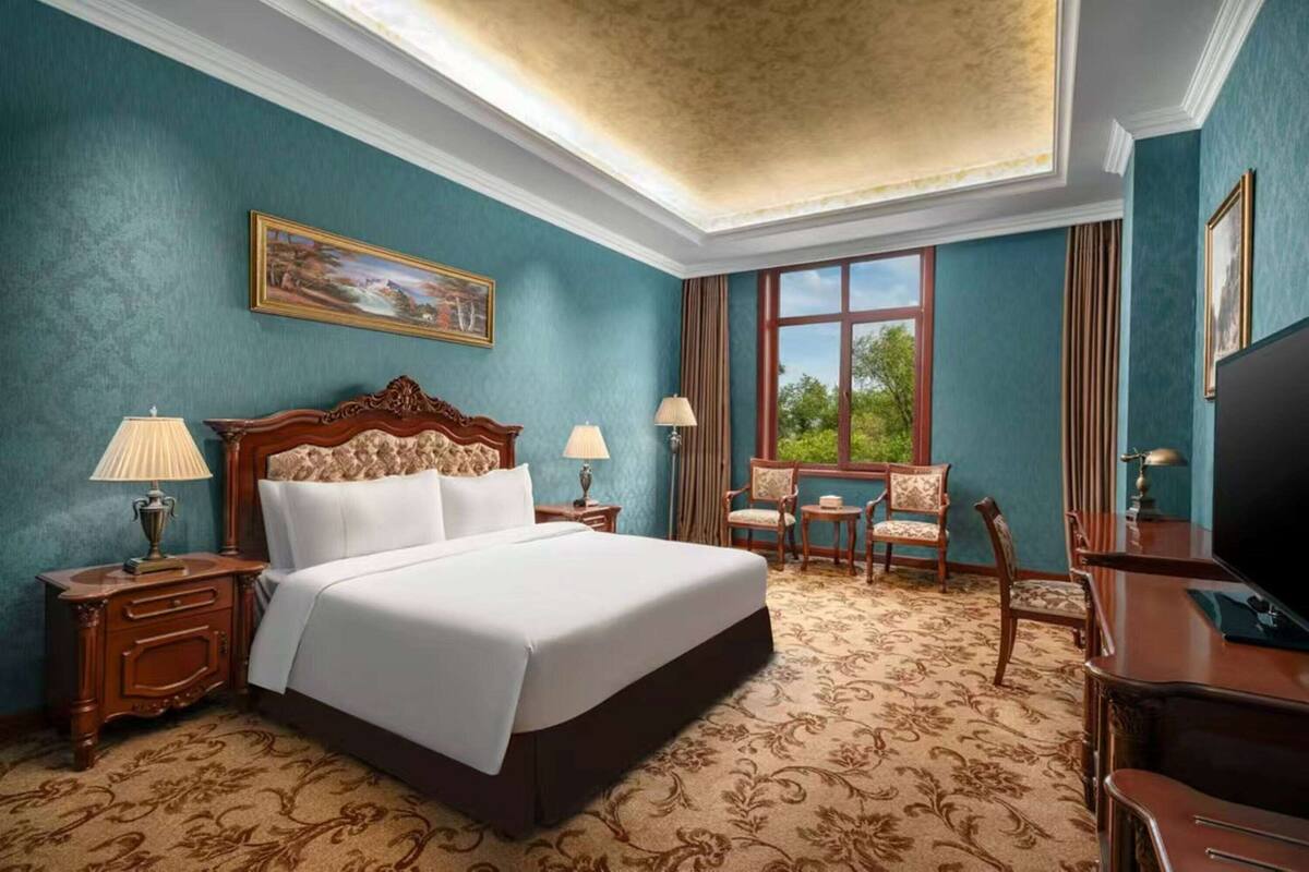 A hotel room with a large bed, two bedside tables with lamps, a desk with a chair, and a television.
