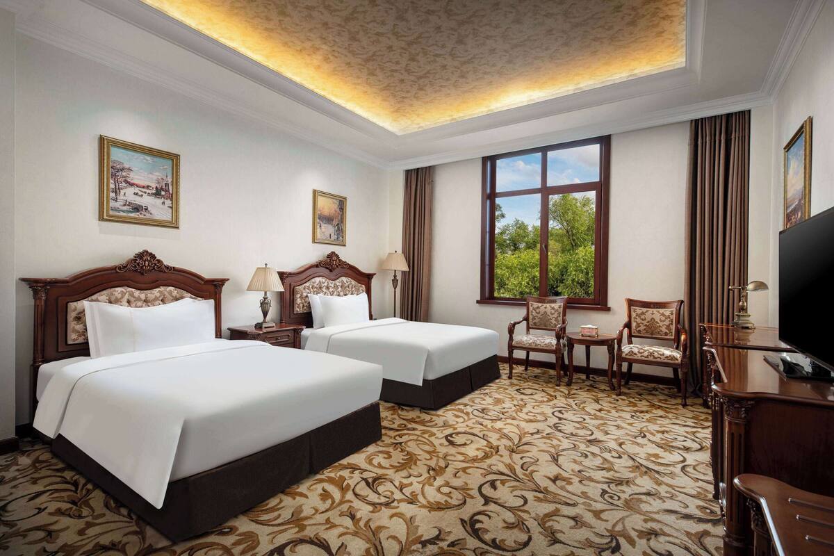 A hotel room with two beds, a desk, a chair, and a television.