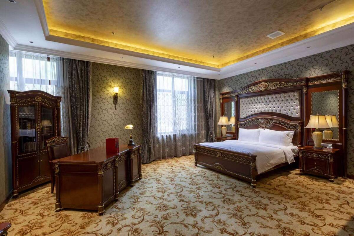 A spacious hotel room with a large bed, a wooden desk, and a cabinet.