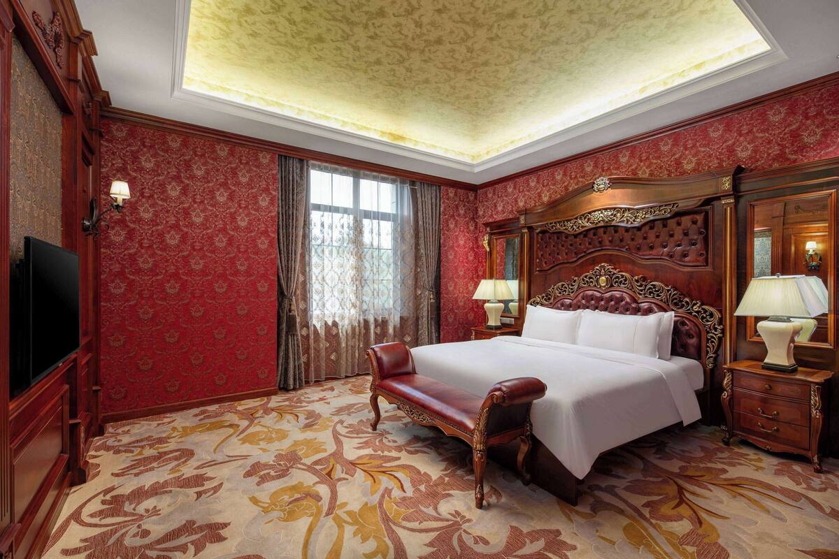 A spacious bedroom with a large bed, a bench, and a television.