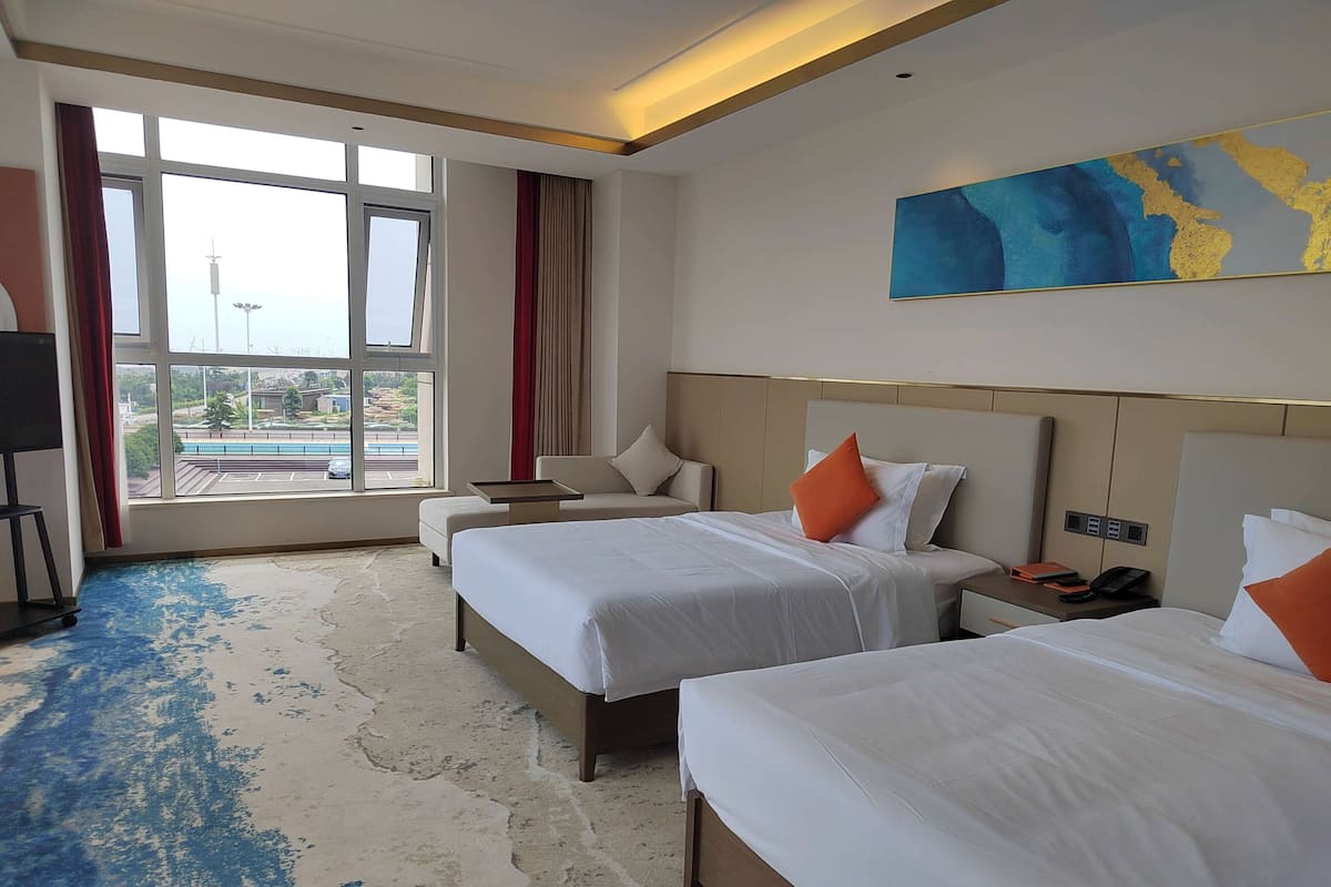 A hotel room with two beds, a large window with a view, a flat-screen TV, and a painting on the wall.