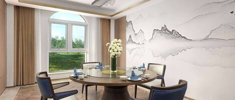 A dining area with a round table, chairs, a vase of flowers, and a wall with a mountain painting.