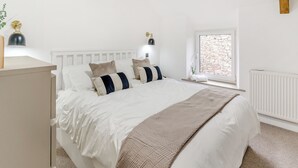 Ein Schlafzimmer mit Bett, Nachttischlampen, einem Fenster mit Blick auf eine Steinmauer und einer Heizung.
