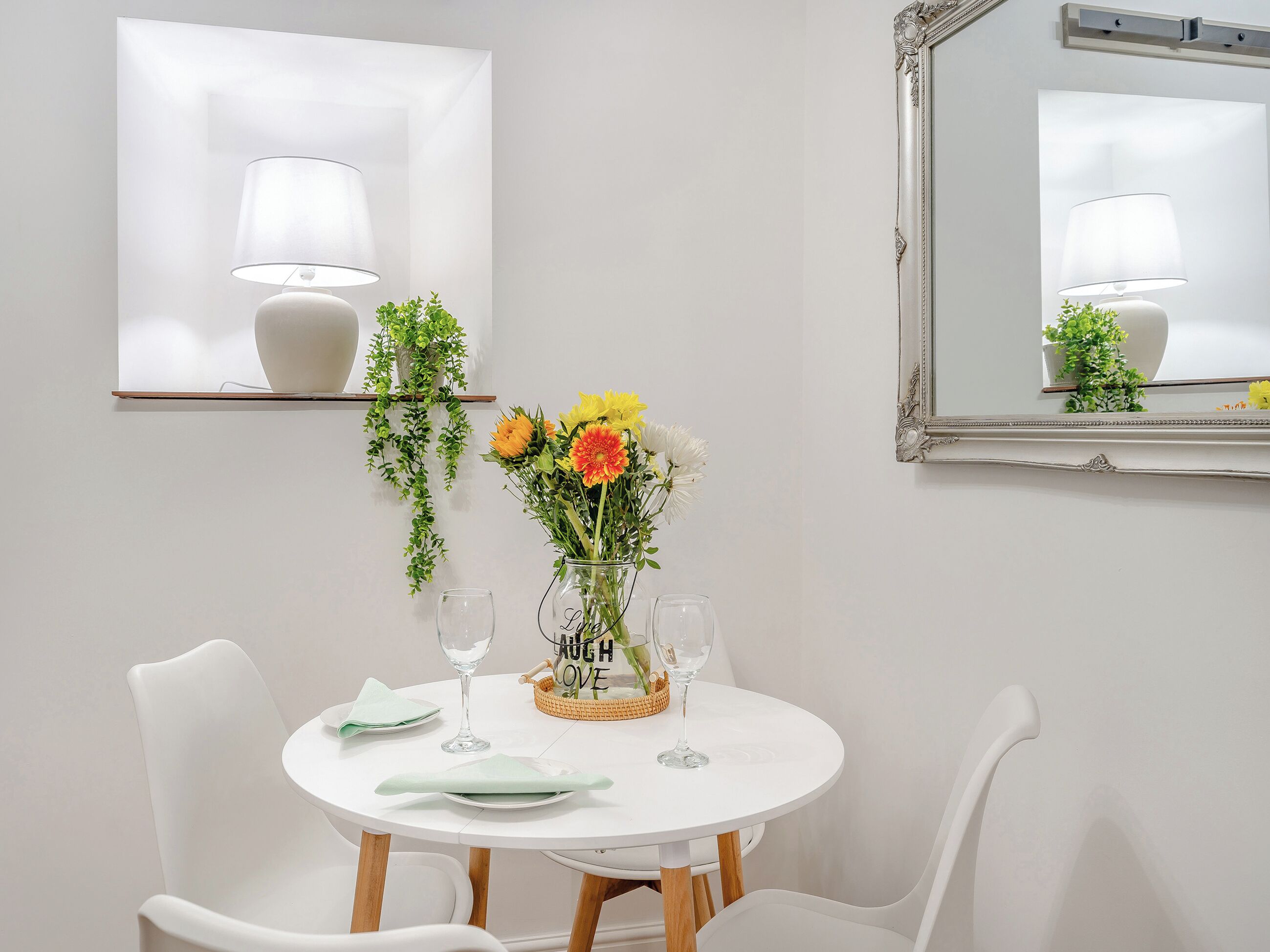 A dining table with chairs, a vase of flowers, a basket, and a mirror on the wall.