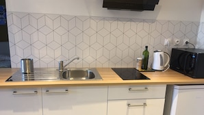 A modern kitchen with a stainless steel sink, a kettle, a microwave, and a coffee maker on the countertop.