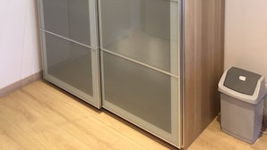 A room with a large, modern, glass-fronted wardrobe and a small trash bin.