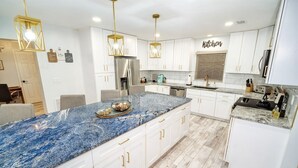 A modern kitchen with white cabinets, a granite countertop, and gold pendant lights. - The Lily Pad- Pool Table Home (Tampa)