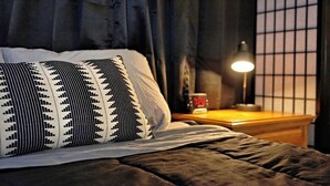 A neatly made bed with a patterned pillow, a bedside lamp, and a clock on a wooden nightstand. - The Lily Pad- Pool Table Home (Tampa)