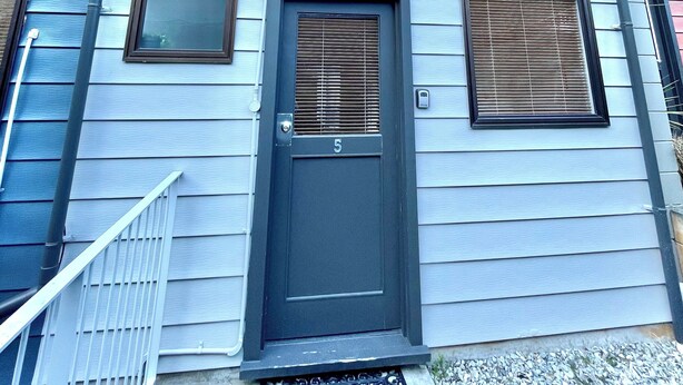 A two-story house with a dark front door, two windows with blinds, and a small porch with a metal railing. - OK Holiday Unit #5 - Queenstown Holiday Apartment (Queenstown)