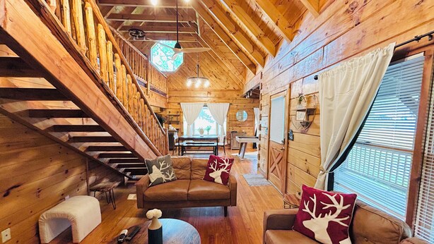 L’intérieur d’un chalet en bois, avec un escalier, un canapé, une table et une fenêtre équipée de stores.
