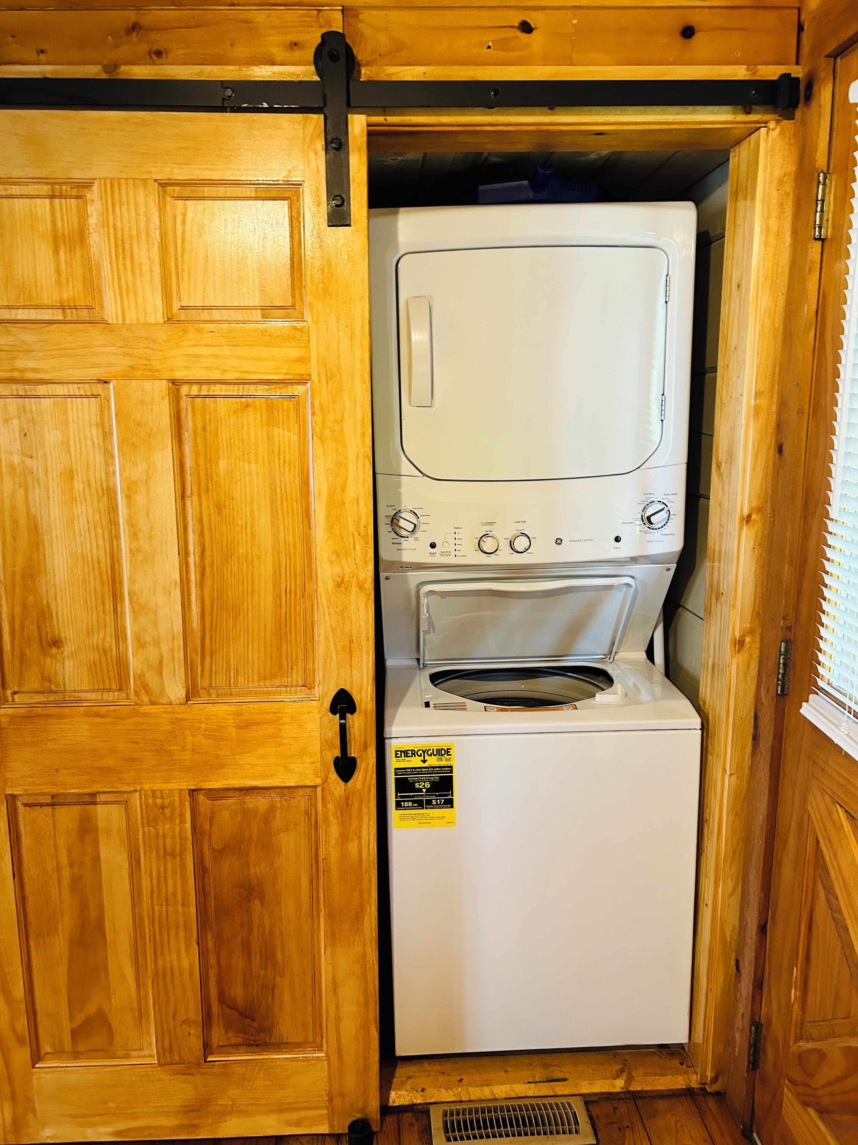 A compact, white laundry room with a built-in washer and dryer, wooden walls, and a vent at the bottom.