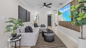 Un salon moderne avec un canapé gris, une table basse noire et un grand tableau représentant une scène de plage.