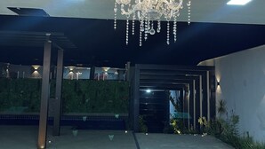 A modern building with a large chandelier, a covered entrance, and a landscaped area. - Espaço de Festas e Descanso Cintia Lima (Petrovale Betim)