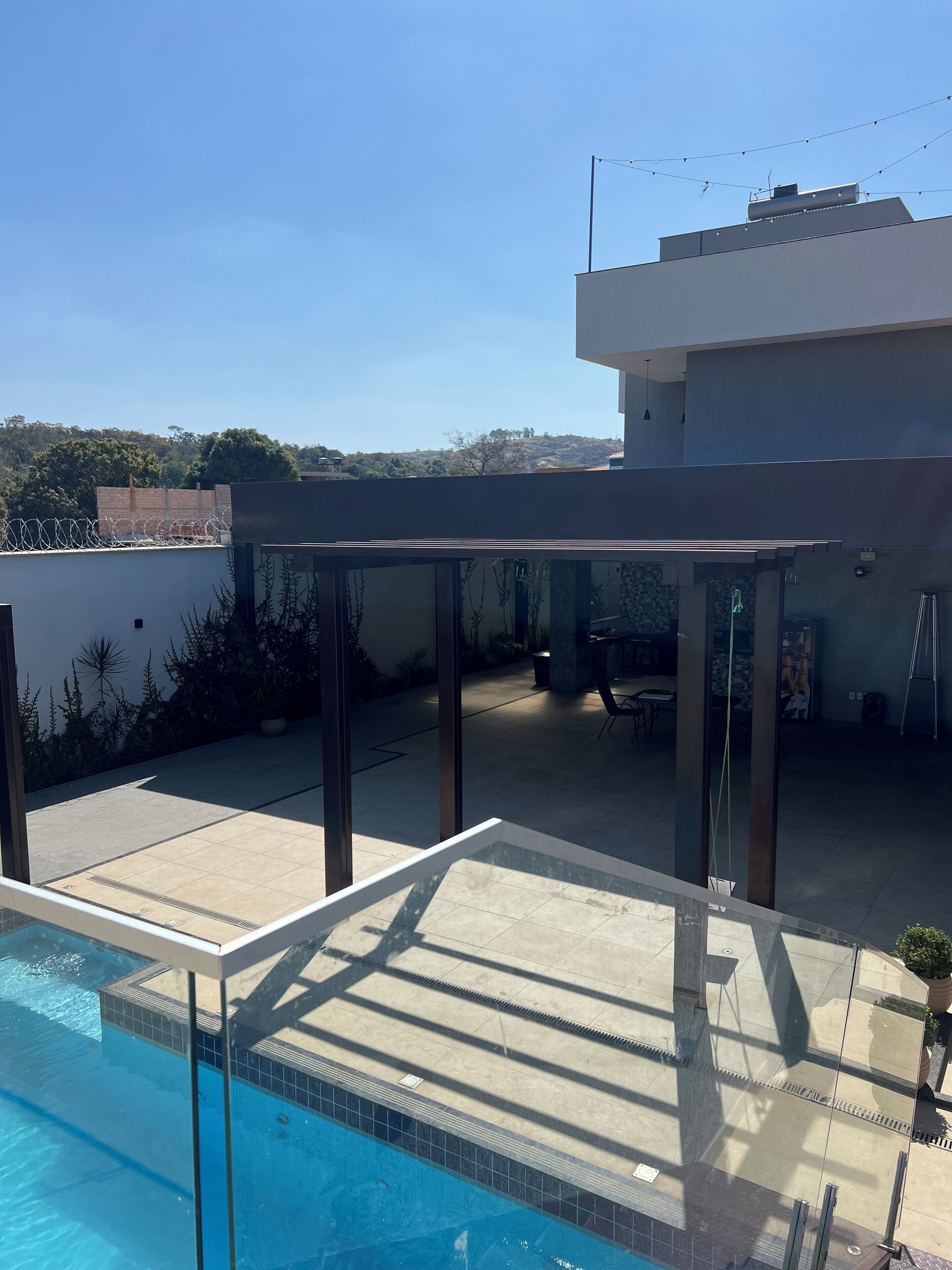 Un área de piscina exterior moderna con vistas despejadas del paisaje circundante, una zona de estar cubierta y un edificio con techo plano.