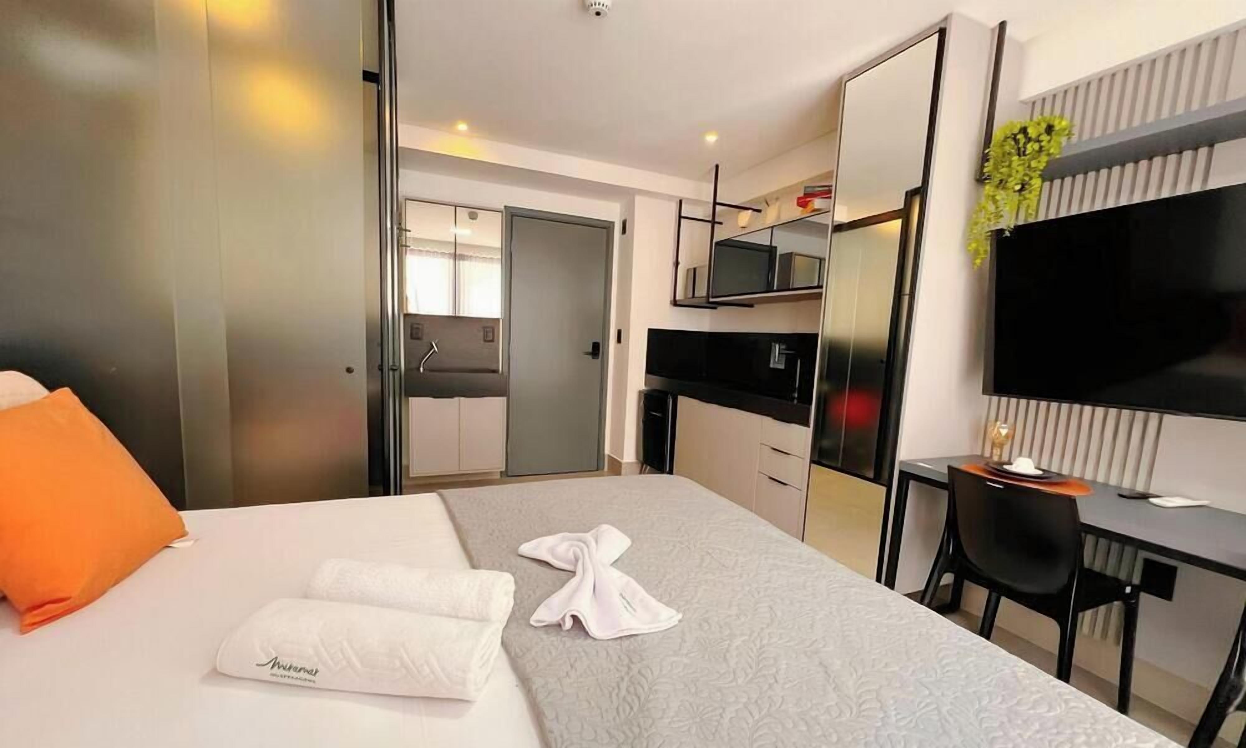 A modern hotel room with a bed, a desk, a TV, and a bathroom visible through a door.