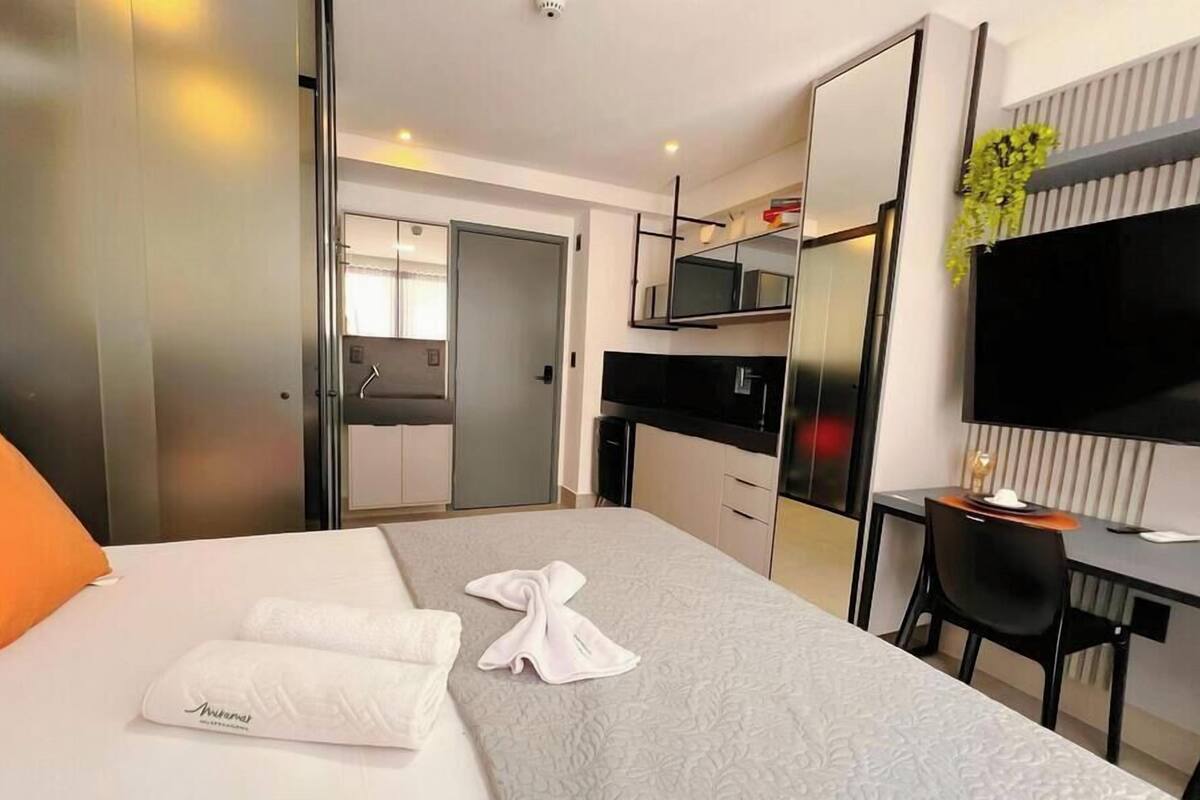 A hotel room with a bed, a desk, a TV, and a door leading to a bathroom.