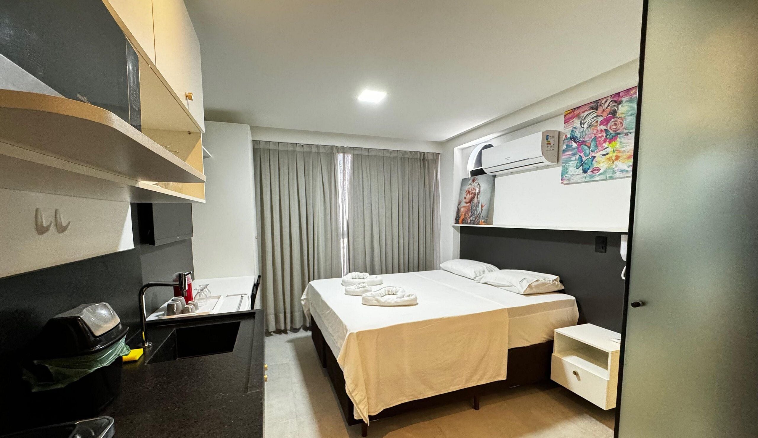 A hotel room with a bed, a desk, a trash bin, a shower area, and a bathroom.