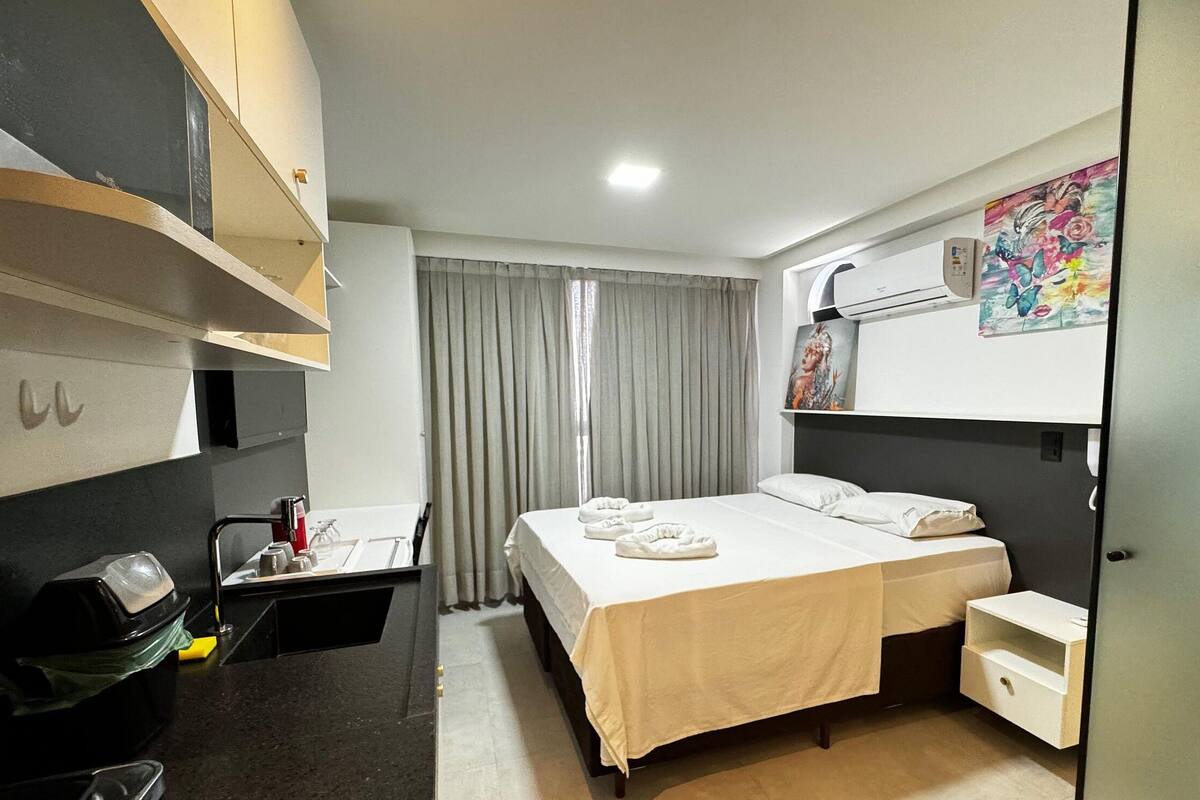 A hotel room with a bed, a desk, a trash bin, a shower area, and a bathroom.
