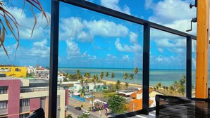 A view from a high-rise building overlooking a beach with palm trees and a clear sky. - Get By Side  (João Pessoa)