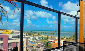 A view from a window overlooking a beach with palm trees and a clear sky. - Get By Side  (João Pessoa)