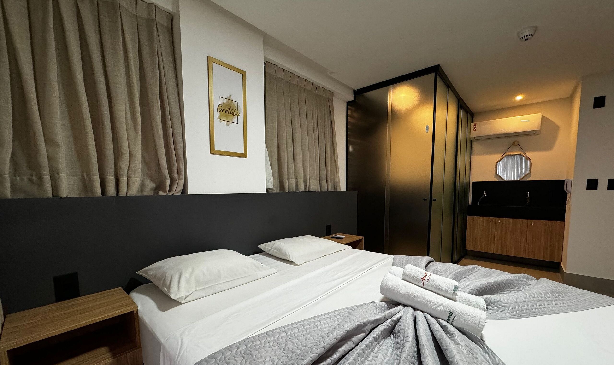 A hotel room with a bed, a bedside table, a wardrobe, and a bathroom with a mirror and towel rack.