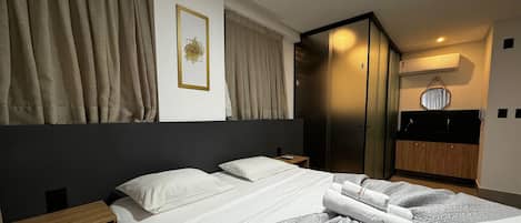 A hotel room with a bed, a bedside table, a wardrobe, and a bathroom with a mirror and towel rack.