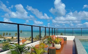 Un balcon avec vue sur l’océan et la plage, agrémenté de plantes en pot et de mobilier d’extérieur.