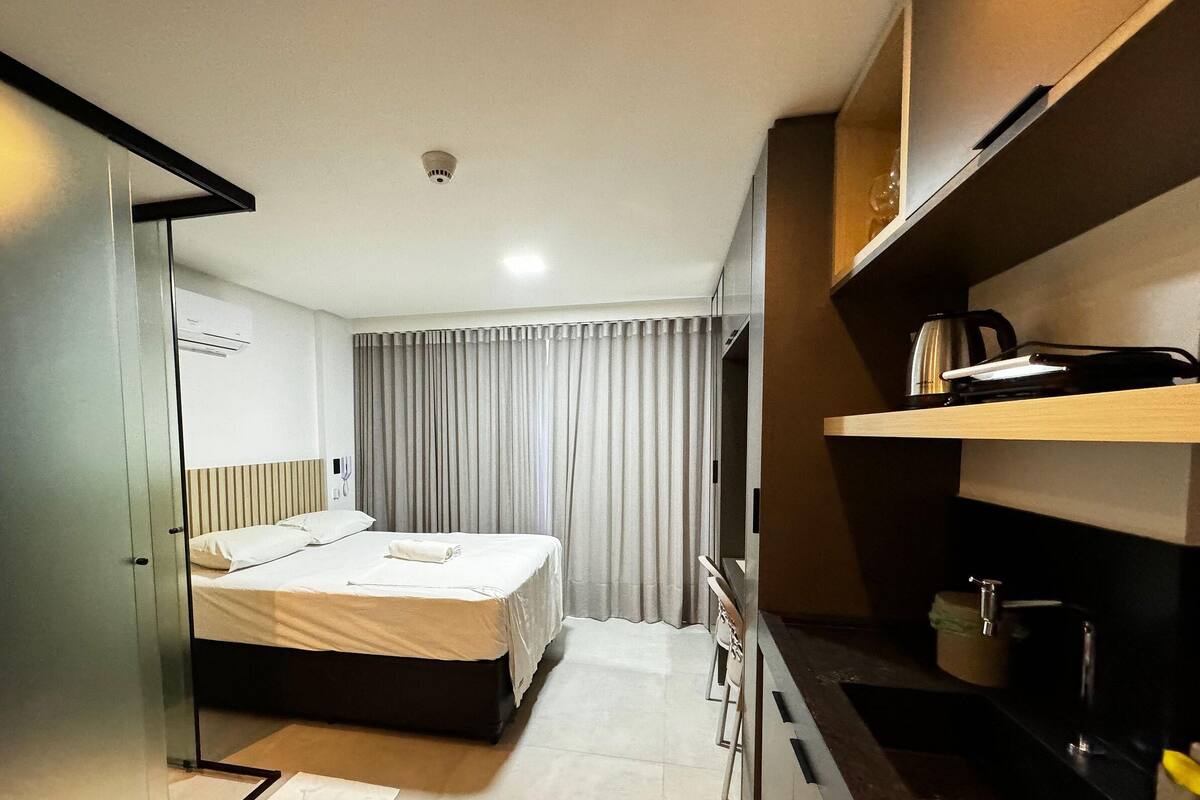 A hotel room with a bed, a desk, a chair, a coffee maker, and a curtain.