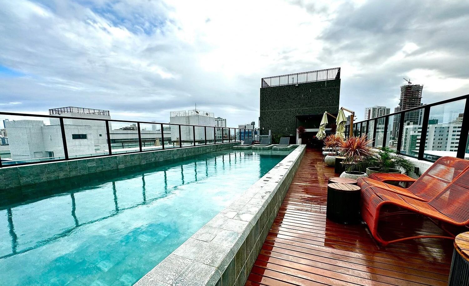 A rooftop pool with a view of the city skyline, wooden deck, and outdoor seating area.