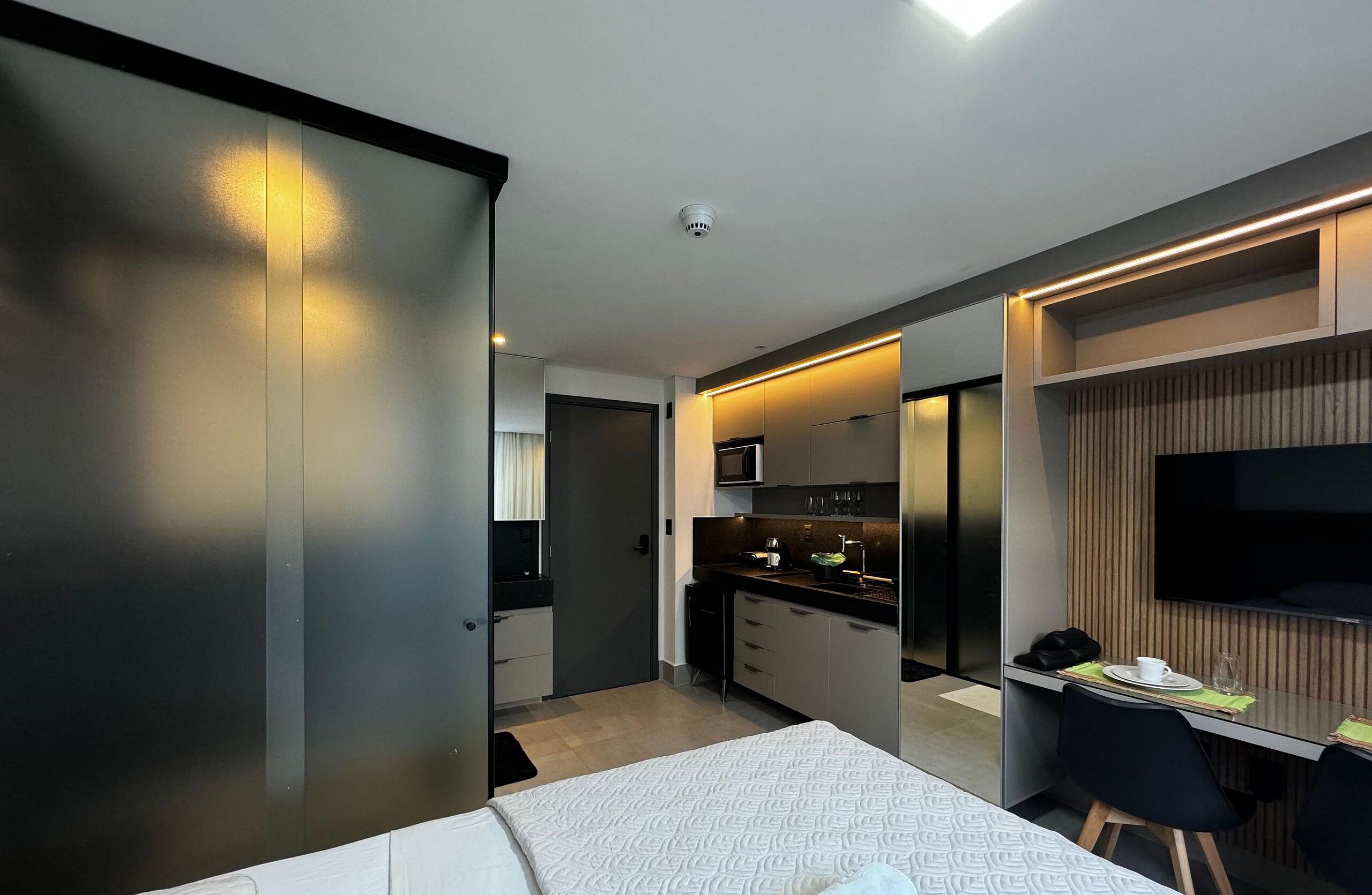 Una habitación de hotel moderna con una cama, un escritorio con una silla, una kitchenette y un televisor.