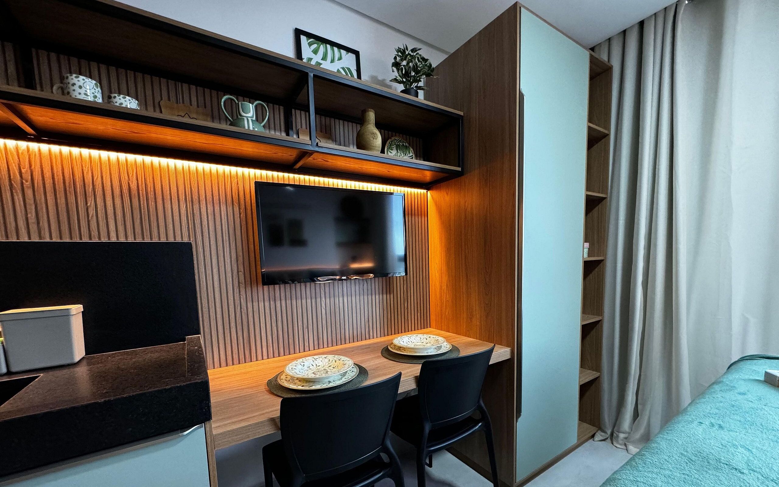Une cuisine moderne dotée d’un téléviseur encastré, de meubles en bois et d’un coin repas avec deux chaises et une table.