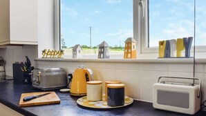 Una cocina con vista al exterior, un tostador, un hervidor, una radio y una tabla de cortar.