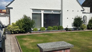 Una casa de dos pisos con fachada blanca, una chimenea de ladrillo y un garaje con puerta metálica.