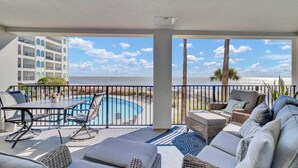 A balcony with a pool, lounge chairs, and a view of the ocean.