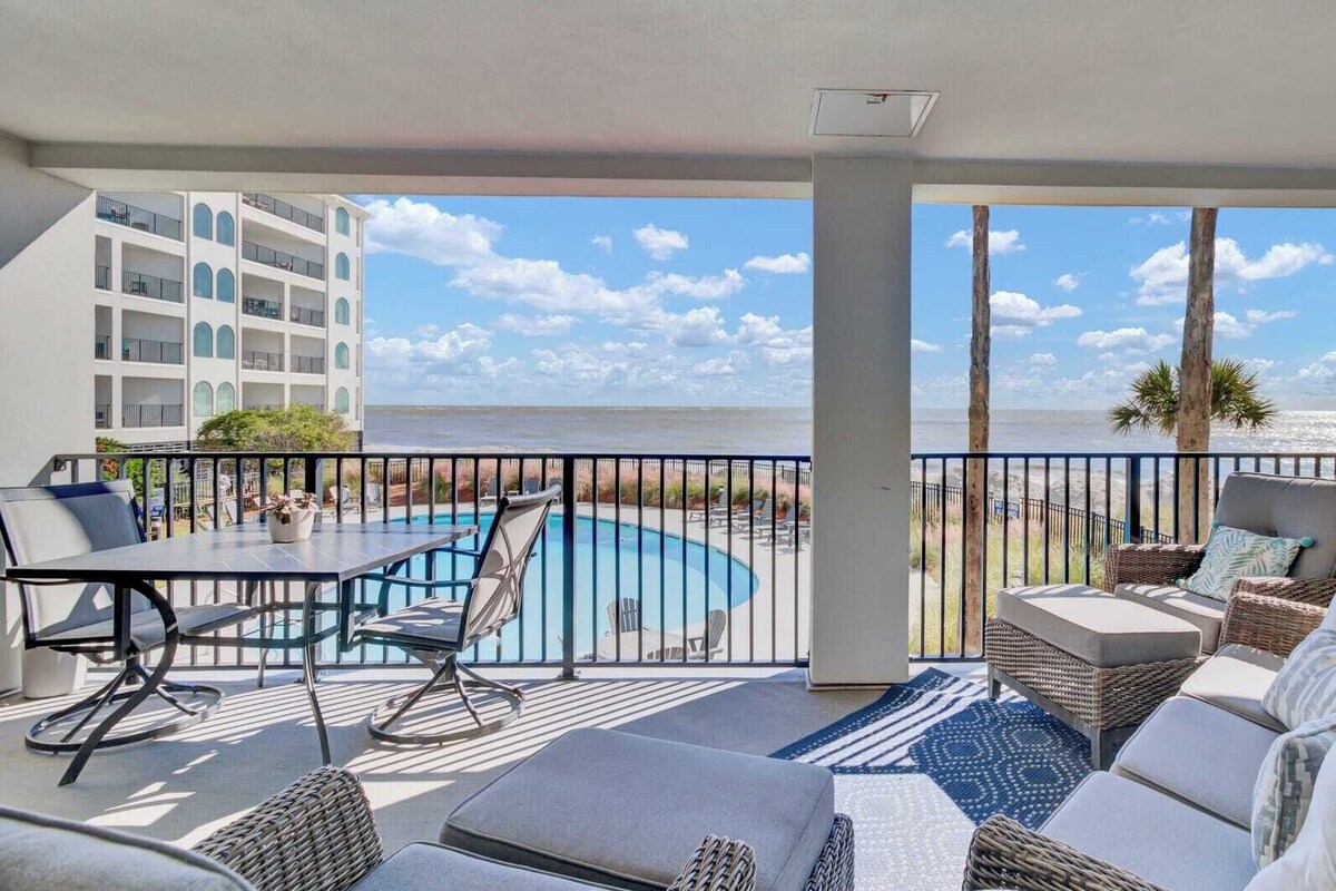 A balcony with a pool, lounge chairs, and a view of the ocean.