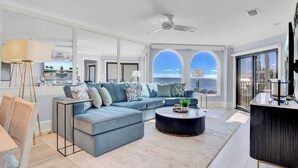 A modern living room with a large sectional sofa, a round coffee table, and a view of the ocean through large windows.