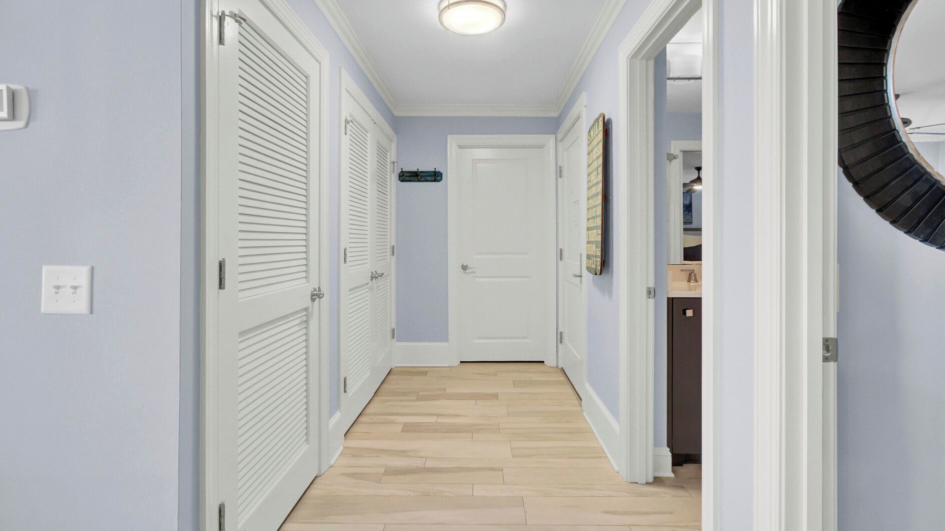 A hallway with white doors, a light blue wall, and a wooden floor.