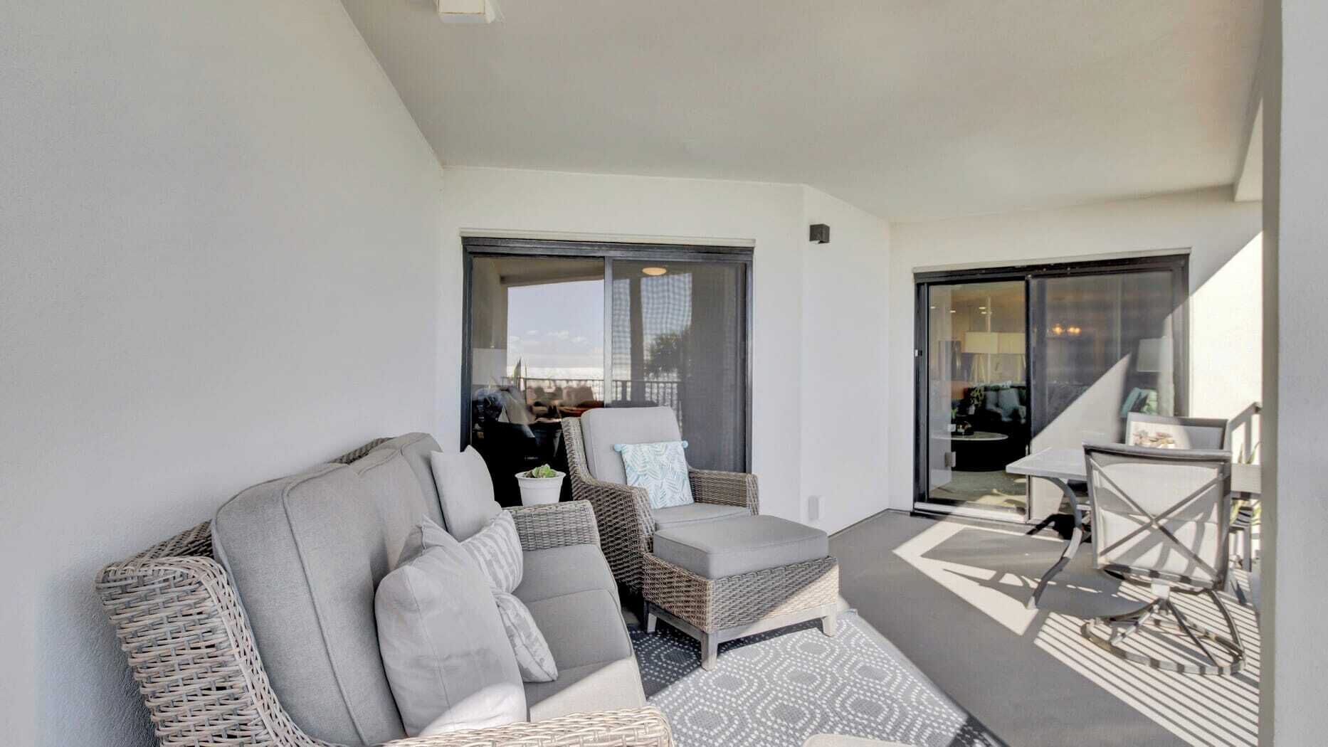 A modern living room with a sofa, armchairs, and a small table. There is a sliding glass door leading to a balcony.