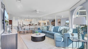 A modern living room with a blue sofa, a round coffee table, and a kitchen in the background. - 118 Seascape by Avantstay Pool + Oceanfront Views (Isle of Palms)