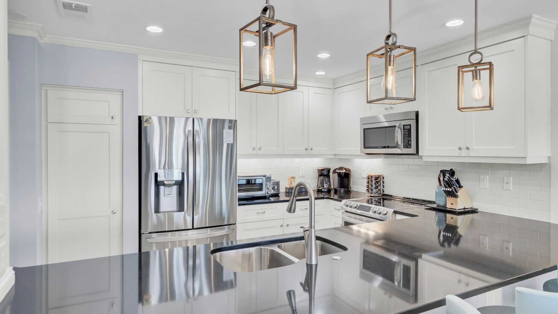 Une cuisine moderne dotée d’appareils électroménagers en acier inoxydable, d’un îlot central et de luminaires suspendus.