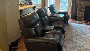 A living room with a sectional sofa, a stone fireplace, and a kitchen area visible through an open door.