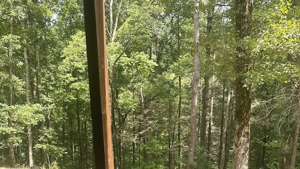 A hot tub in a forested area with a wooden deck and a chair.