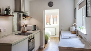 Eine kleine Küche mit Herd, Mikrowelle und Spüle. Ein Fenster sorgt für Tageslicht und einen Ausblick.