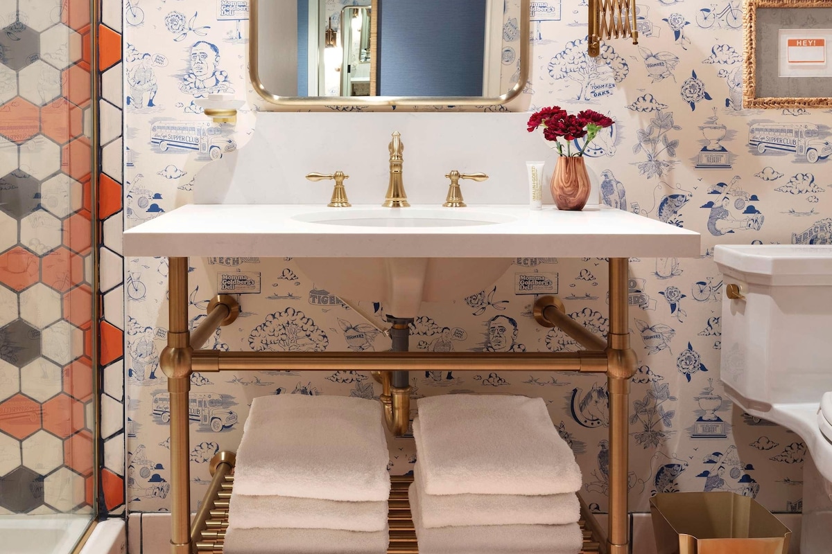 A bathroom with a white sink, gold fixtures, a mirror with lights, and hexagonal patterned walls.