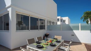 Ein moderner Essbereich im Freien mit einem Tisch für vier Personen, umgeben von Stühlen, und ein großes Fenster mit Blick auf den Himmel und angrenzende Gebäude.