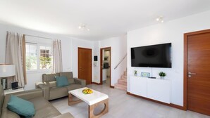 Ein Wohnzimmer mit Sofa, Couchtisch, Fernseher und einer Treppe zu einem anderen Raum.