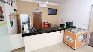 A reception area with a counter, a refrigerator, a freezer, a television, and a door. - Hotel Portela III (Olímpia)