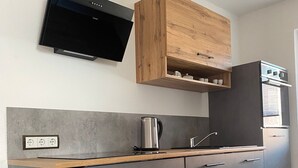A modern kitchen with grey cabinets, a wooden countertop, a built-in stove, and a flat-screen TV mounted above the cabinets. - Ferienwohnung an der Schlösserachse . Ideal für Ausflüge ins Münsterland (Nordkirchen)