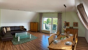 A living room with a sofa, a glass coffee table, a dining table set for four, and a view of the outdoors through a sliding glass door. - Ferienwohnung an der Schlösserachse . Ideal für Ausflüge ins Münsterland (Nordkirchen)