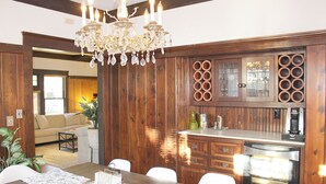 Un espace repas comprenant une table en bois, des chaises, un lustre, ainsi qu’un coin cuisine avec des meubles de rangement en bois et un four encastré.
